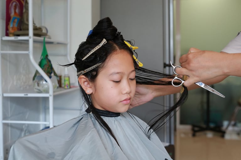 Asian preteen girl having her hair cut. Child sitting in beauty hair salon, close-up of haircut service