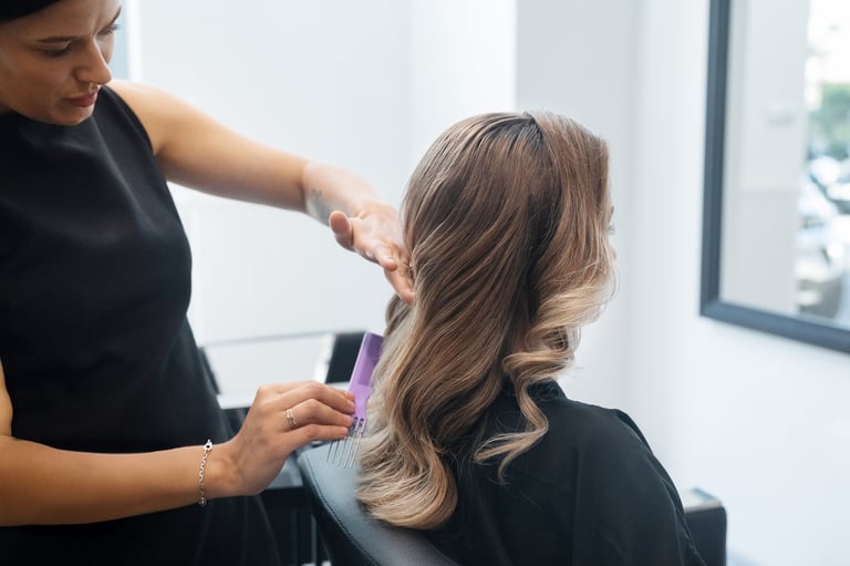 A hairstylist expertly curls a client's hair into soft waves using a comb and styling tools