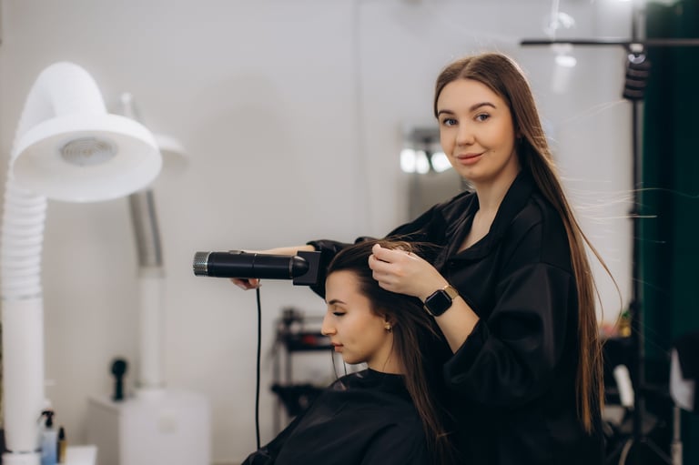 Hairdresser working on client's long brown hair with a blow dryer, providing beauty service in a modern hair salon