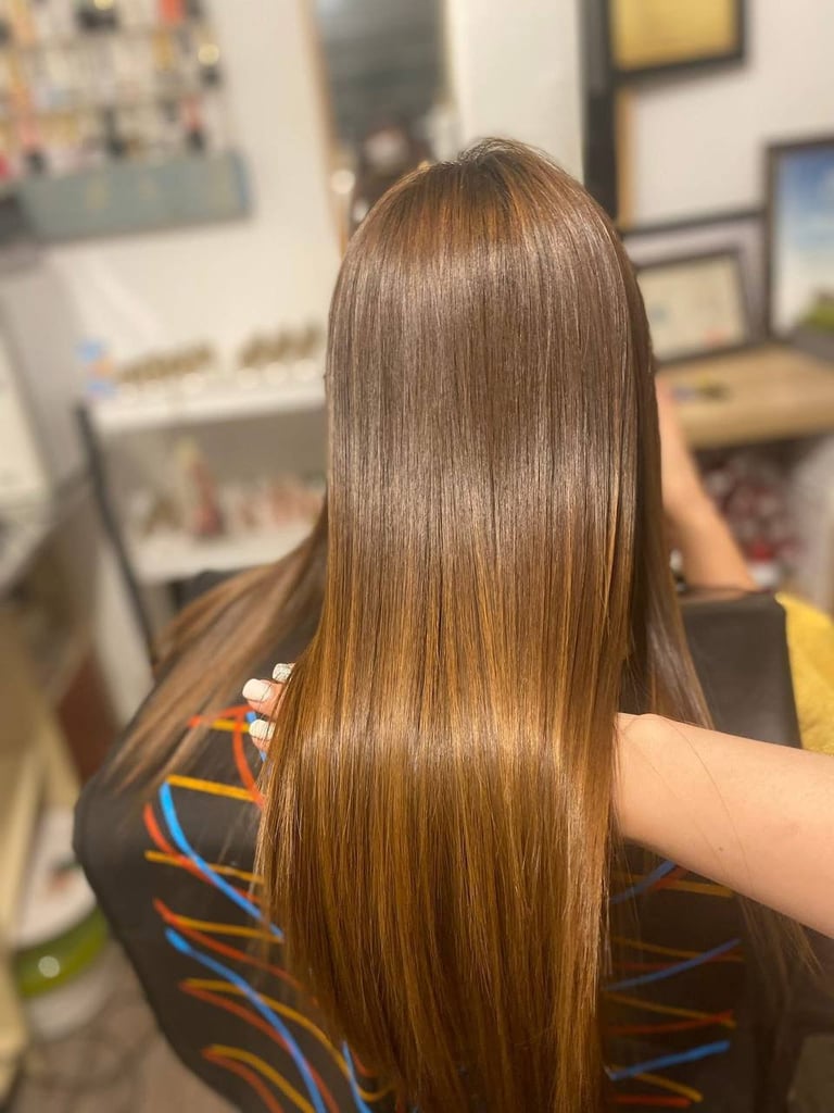 Person with long, straight chestnut brown hair viewed from behind in a salon setting with artwork on the walls