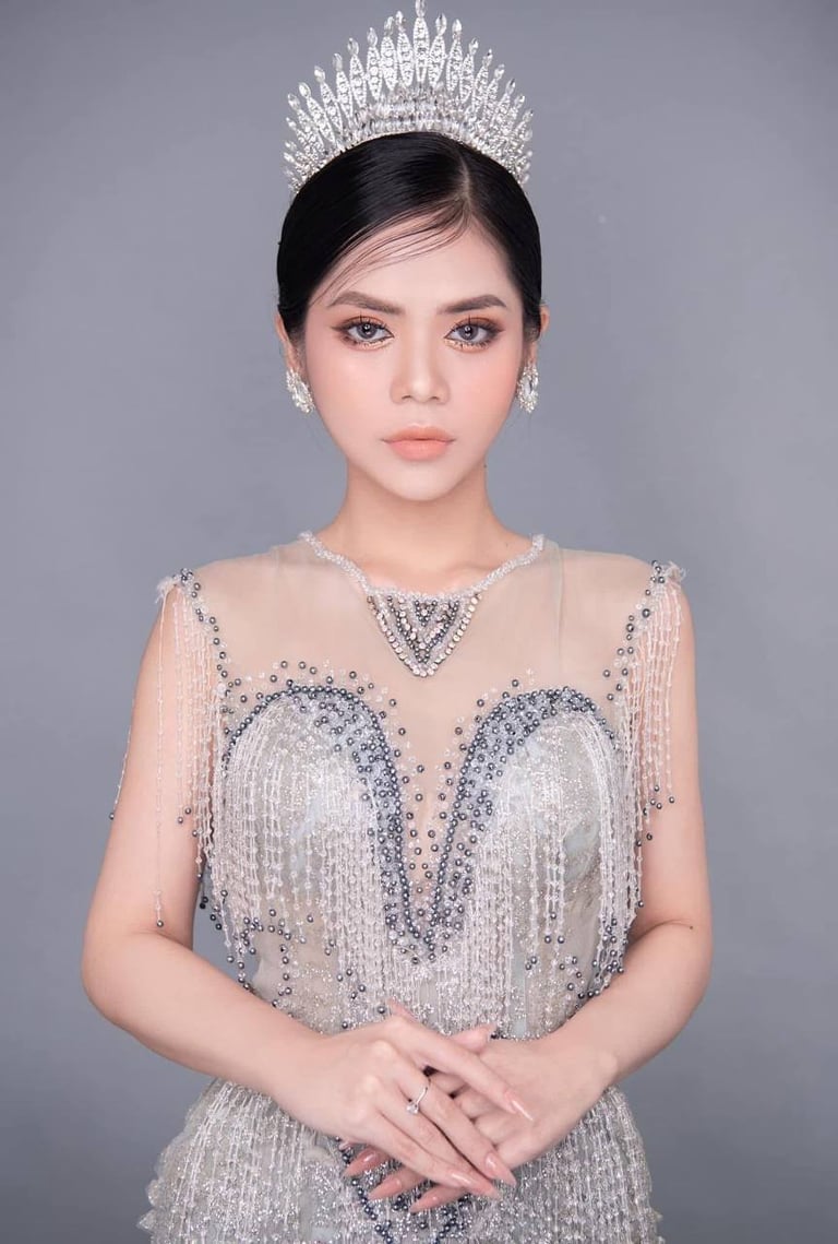 Woman wearing ornate silver tiara and embellished beaded gown against gray background