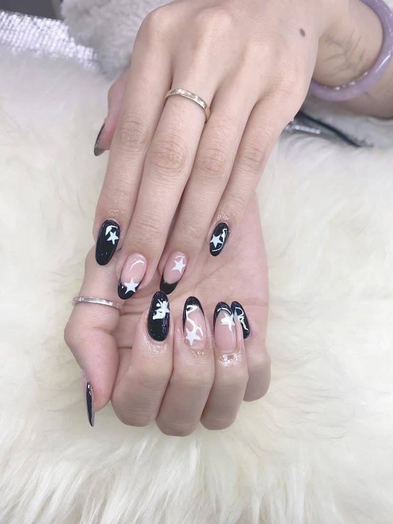 Close-up of manicured hands with black and pink ombre nail art design, wearing silver rings, displaying artistic nail polish