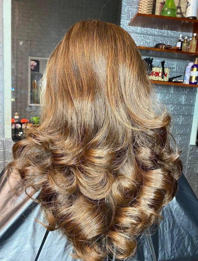 Back view of a woman with long, voluminous golden brown hair styled in loose waves and curls at a salon