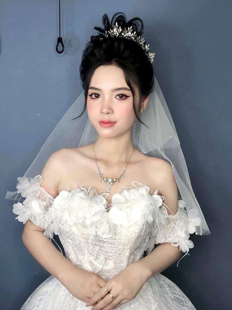 Woman in white wedding dress with ornate tiara, veil, and crystal necklace against blue background