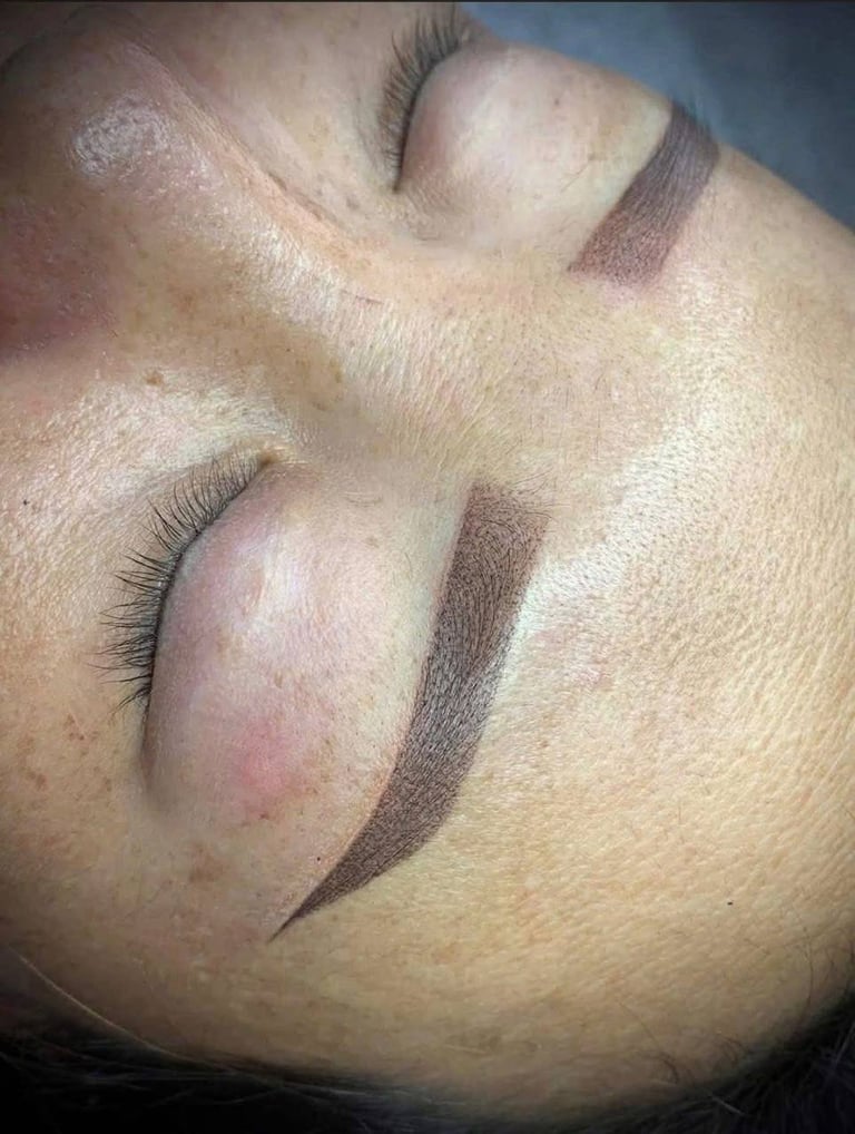 Close-up of a womans face showing eyebrow and eyelash microblading or permanent makeup application with brown pigmentation