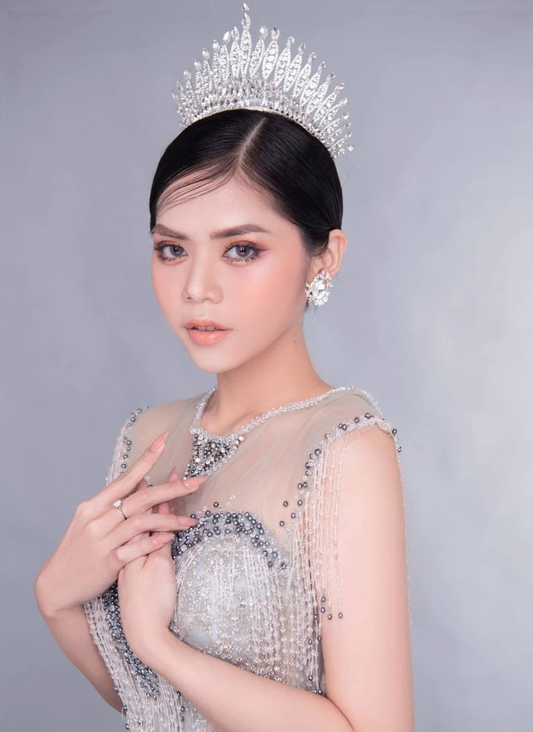 Woman wearing elegant silver beaded gown with ornate tiara and diamond earrings against gray background