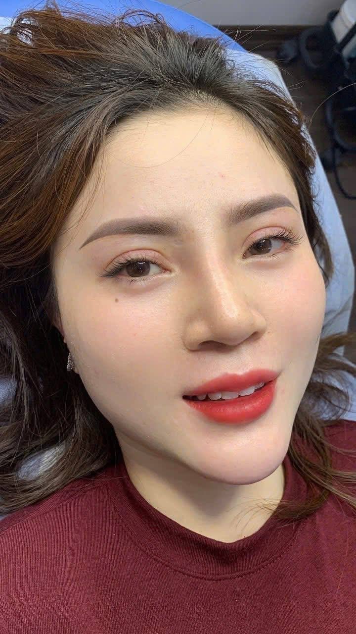 Close-up portrait of a woman with brown wavy hair, wearing red lipstick and a burgundy shirt, smiling at the camera