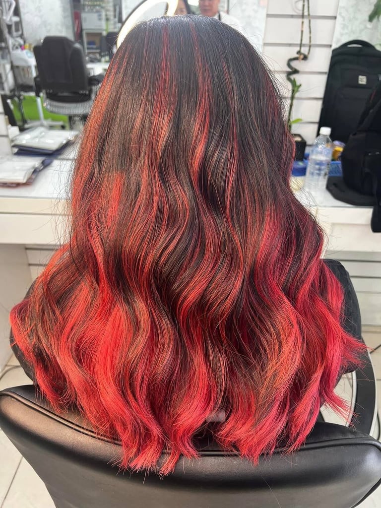 Back view of woman with long wavy hair featuring red and pink ombre highlights in a salon setting