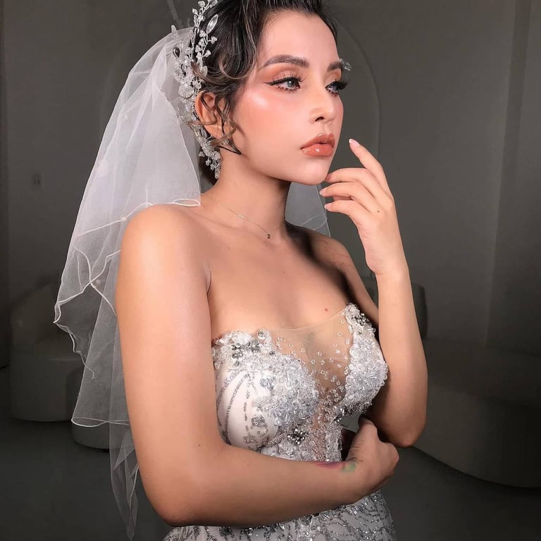 Woman in elegant white sequined wedding dress with ornate veil and jewelry, posing against gray background