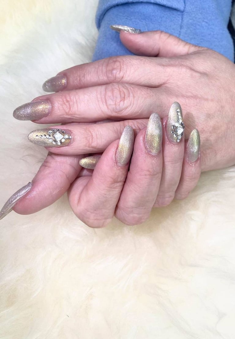 Close-up of two hands with manicured nails featuring sparkly gold and silver glitter polish against a white fluffy background