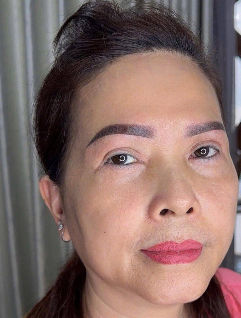 Portrait of a woman with dark pulled-back hair, bold pink lipstick, and defined eyebrows, looking directly at camera indoors