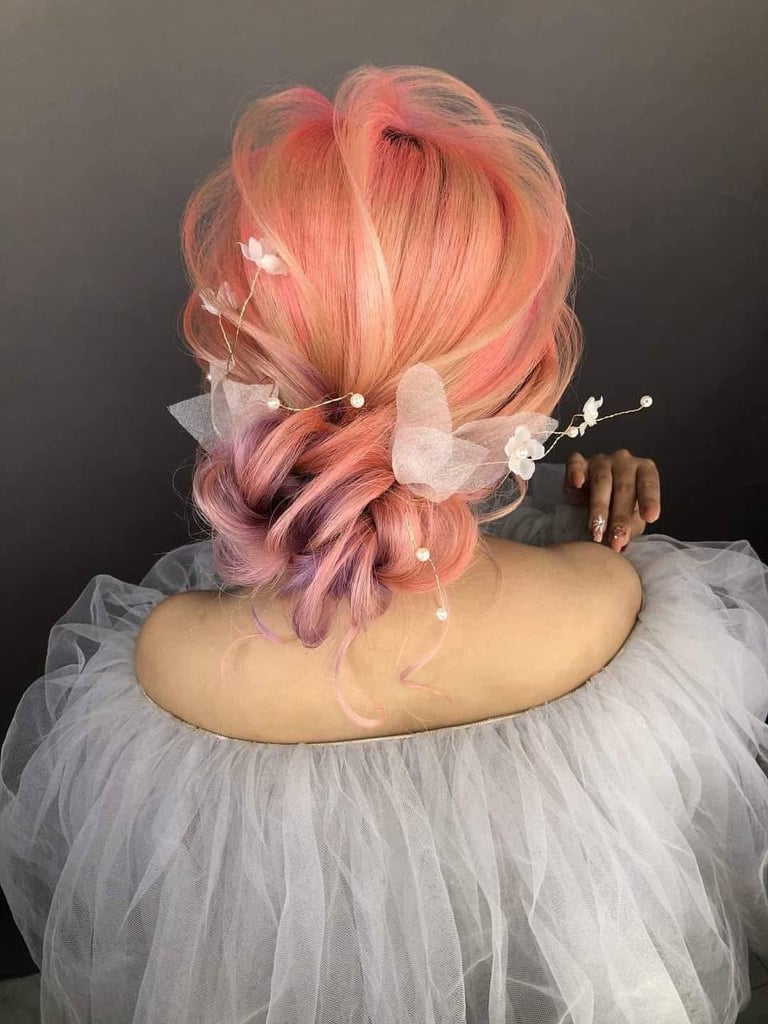 Mannequin head displaying pink ombre hair in an elaborate updo with white floral and tulle accessories against a dark background