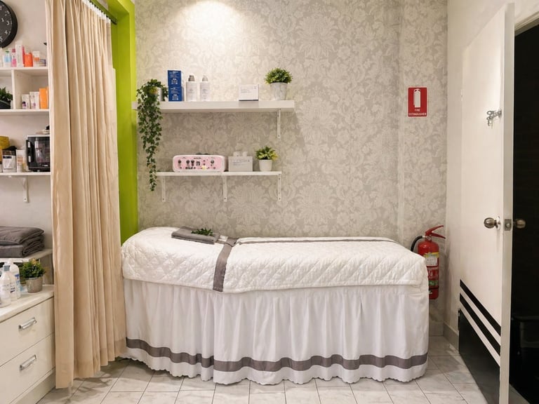 Modern spa massage room with white draped treatment bed, shelving with products, curtains, and minimal decor on beige walls